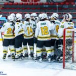 The Australia U18 Women’s Ice Hockey national team celebrates on the ice in their green and gold jerseys.
