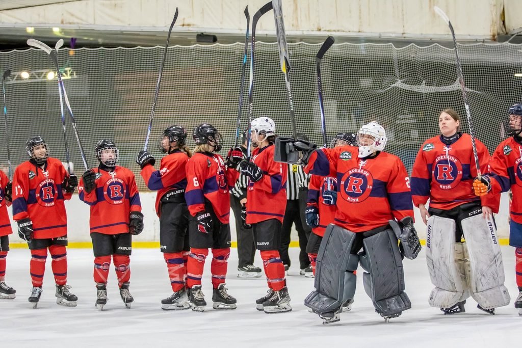 Adelaide Rush ice hockey team players and goaltenders wearing their red and purple uniforms standing together on the ice during a game in the 2025/26 AWIHL season.