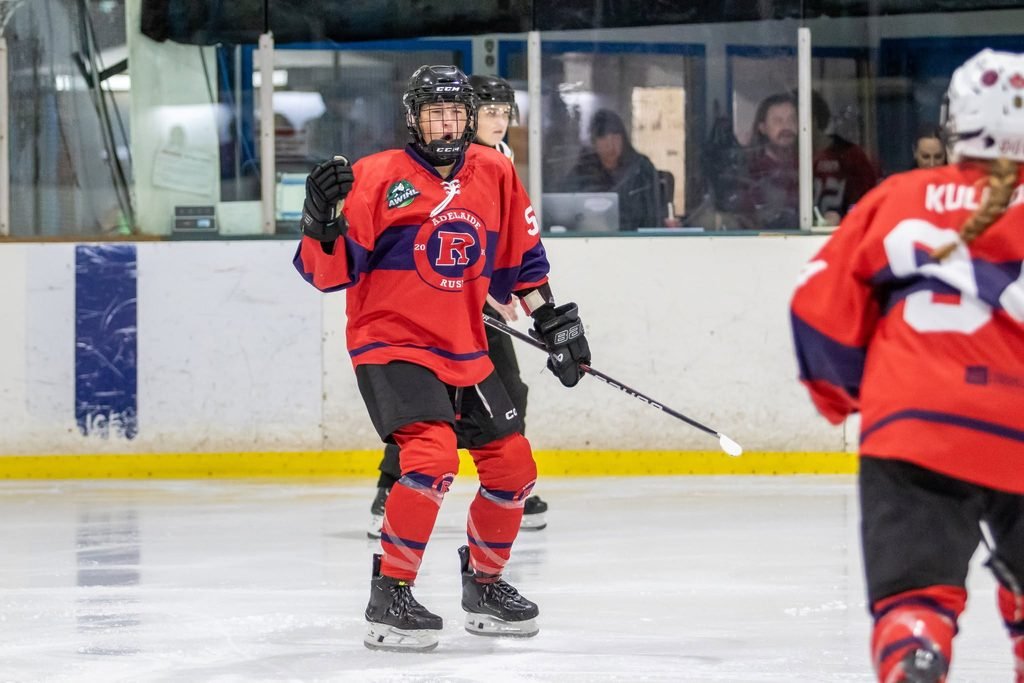 Adelaide Rush ice hockey player Kirsty Venus wearing a red, purple, and blue jersey with the number 59, raising her fist in celebration during an AWIHL game.
