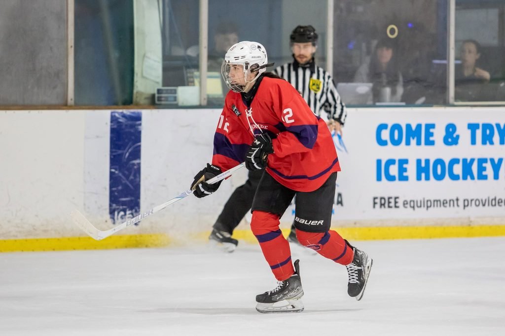 Adelaide Rush ice hockey forward Natalie Ayris wearing a red, white, and blue jersey with the number 12, skating with her stick on the ice during an AWIHL game.
